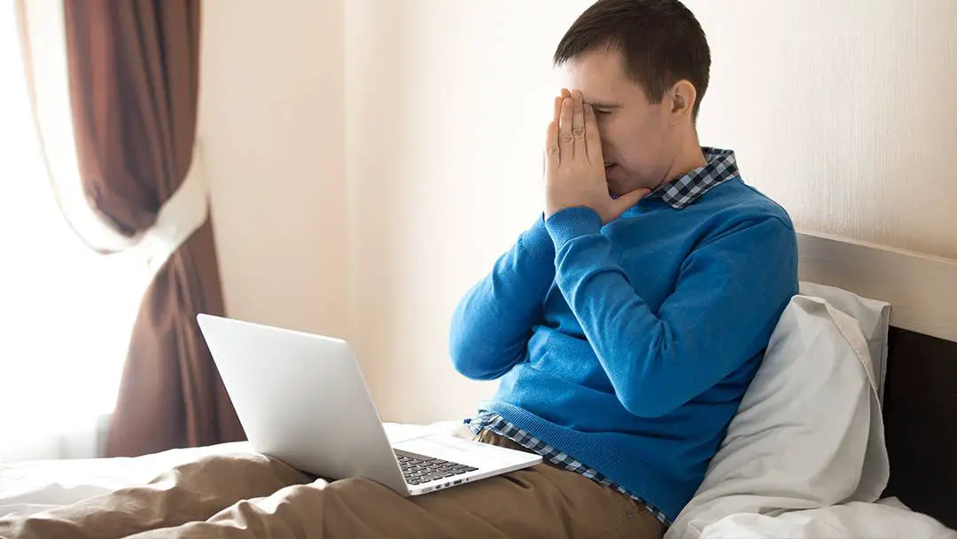 booking woes man sits on bed with head in hands looking at computer
