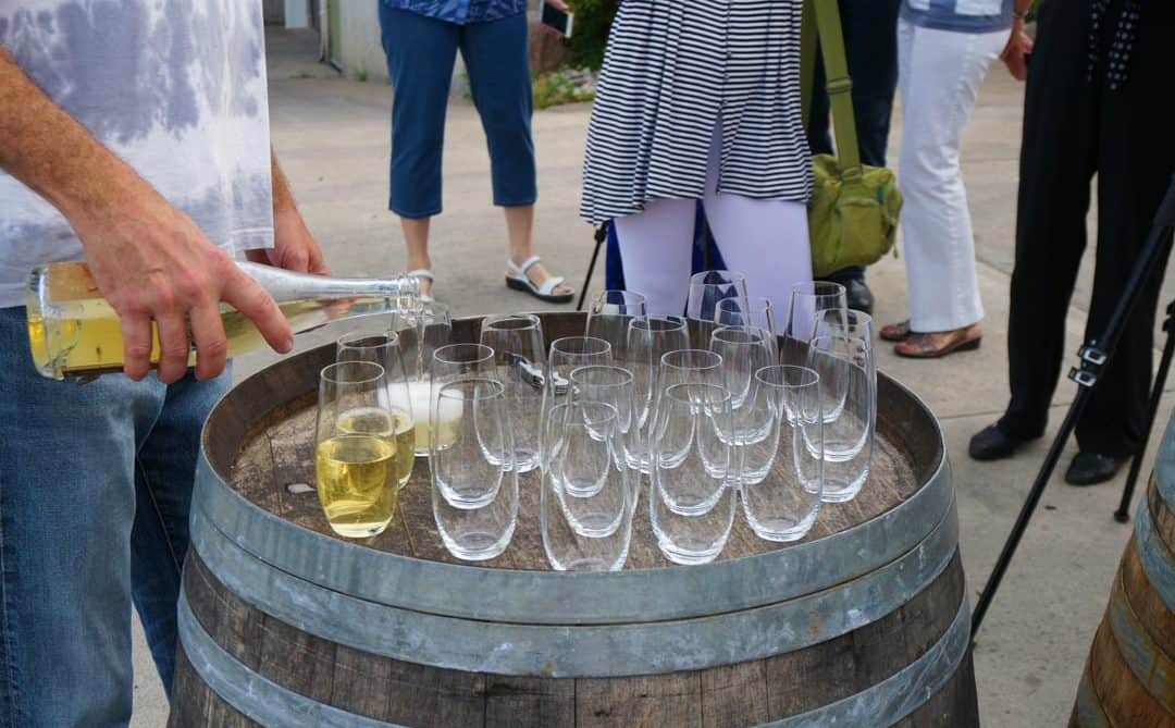 Creekside Winery wine tasting winemaker rob power pours white wine into glasses sitting on a barrel.