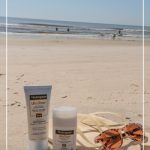 Neutrogena sunscreen products on beach next to flip flops and sunglasses with text Lightweight and Non Sticky Sunscreen A Neutrogena Sunscreen Review