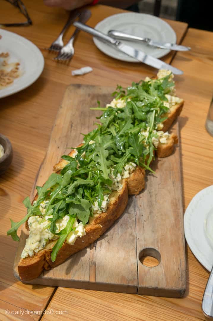Long baguette on board covered with egg salad and greens