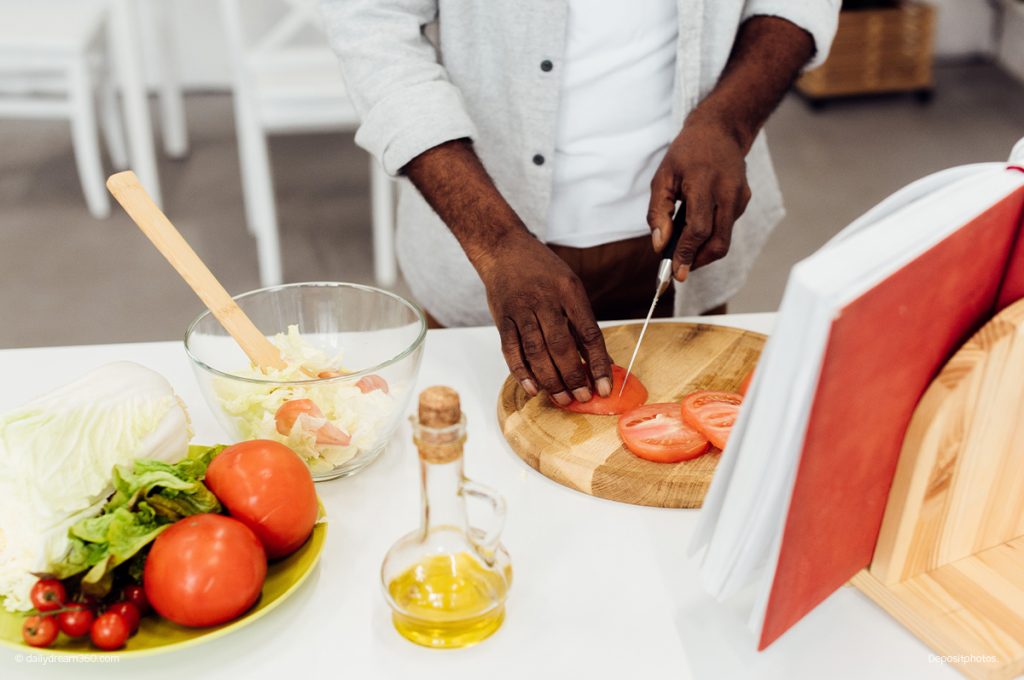 man cutting tomatoes in from of cookbook