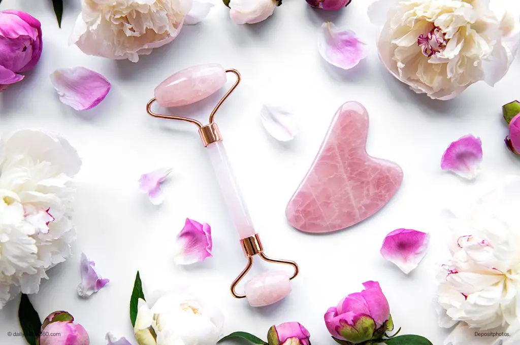 rose quartz face roller on white table with flower petals
