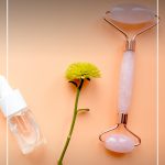 face roller on peach table with flower and text Benefits of a Face Roller and Which Crystal Roller Should You Choose?