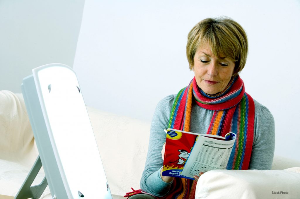 Older woman sitting and reading magazine next to a light therapy box