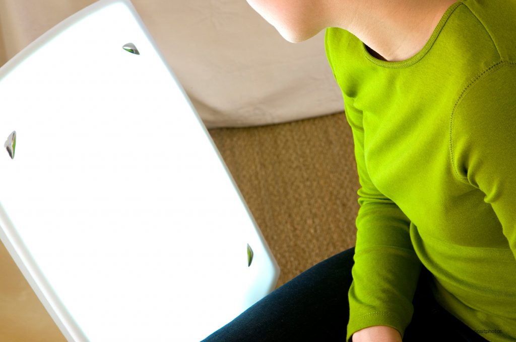 woman in green top looking at light therapy lamp