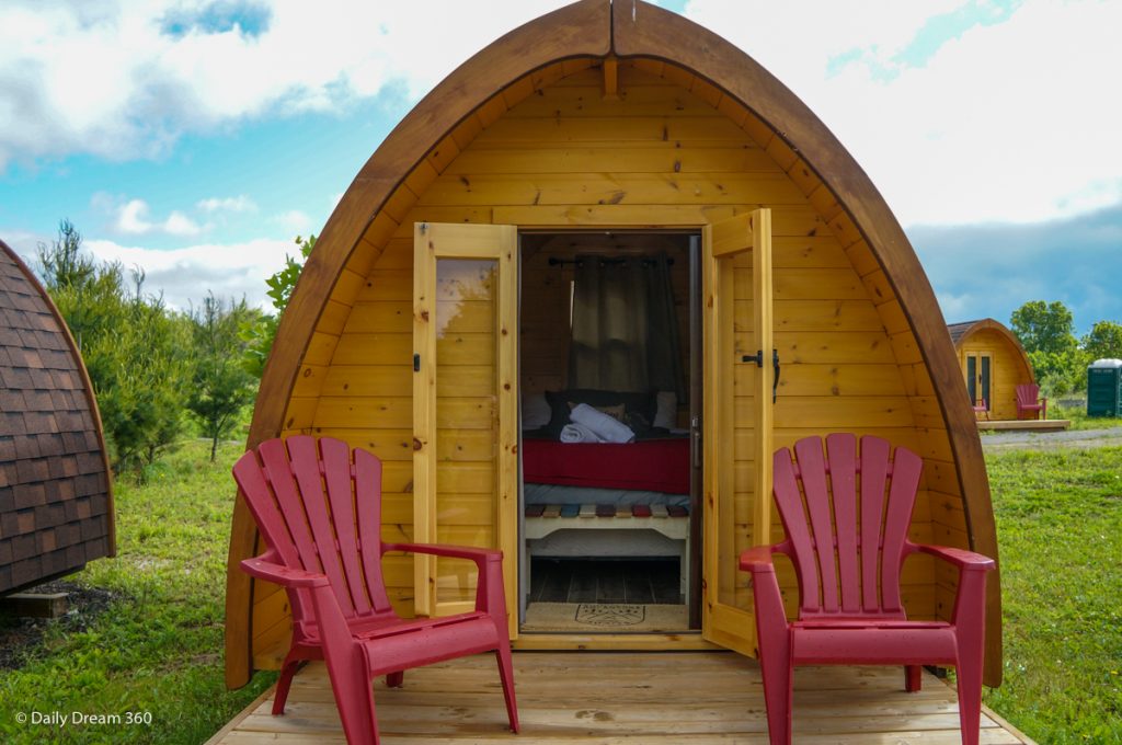 Wilderness Pod with doors open bed inside and two red chairs on deck