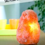 Salt therapy lamp on table with bookcase in background with text: Benefits of Salt Therapy. What You Need to Know About Salt Float Tanks and Salt Caves.