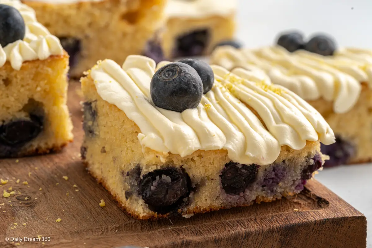 Close up of Keto Blueberry Lemon Cake with No Sugar Cream Cheese Frosting square on wood board