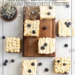 Squares of Keto Blueberry Lemon Cake with No Sugar Cream Cheese Frosting on wood board scattered on counter