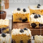 Squares of Keto Blueberry Lemon Cake with No Sugar Cream Cheese Frosting on wood board scattered on counter