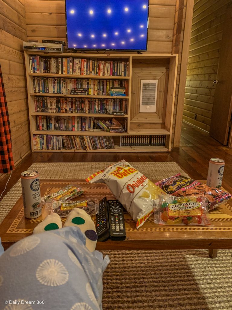 Feet in front of coffee table filled with snacks in front of TV and Video library at Muskoka Beer spa