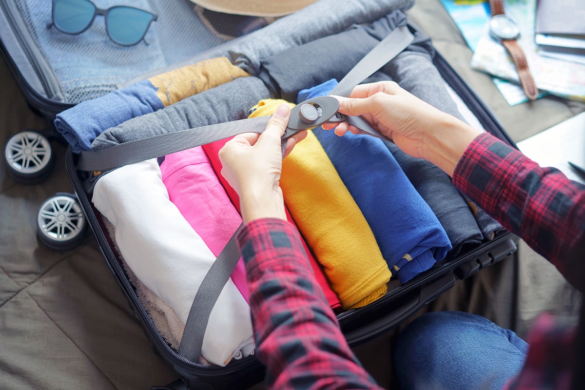 women closing straps on suitcase with rolled clothing