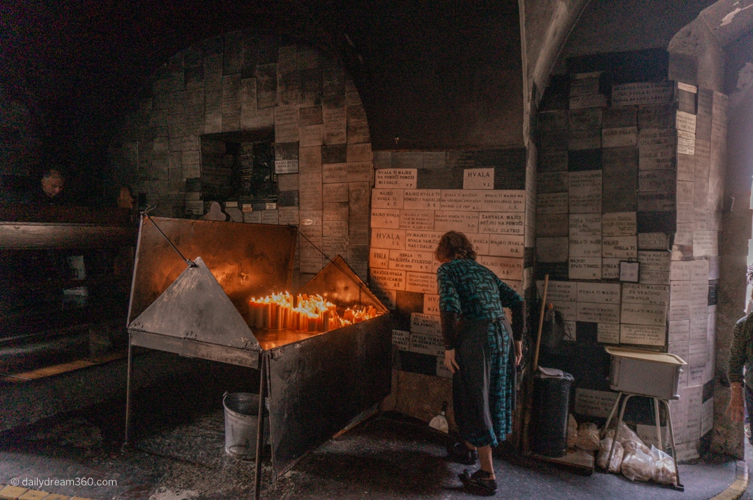 Woman reads bricks on wall in front of candle memorial at the Sacred Stone Gate in Zagreb Croatia